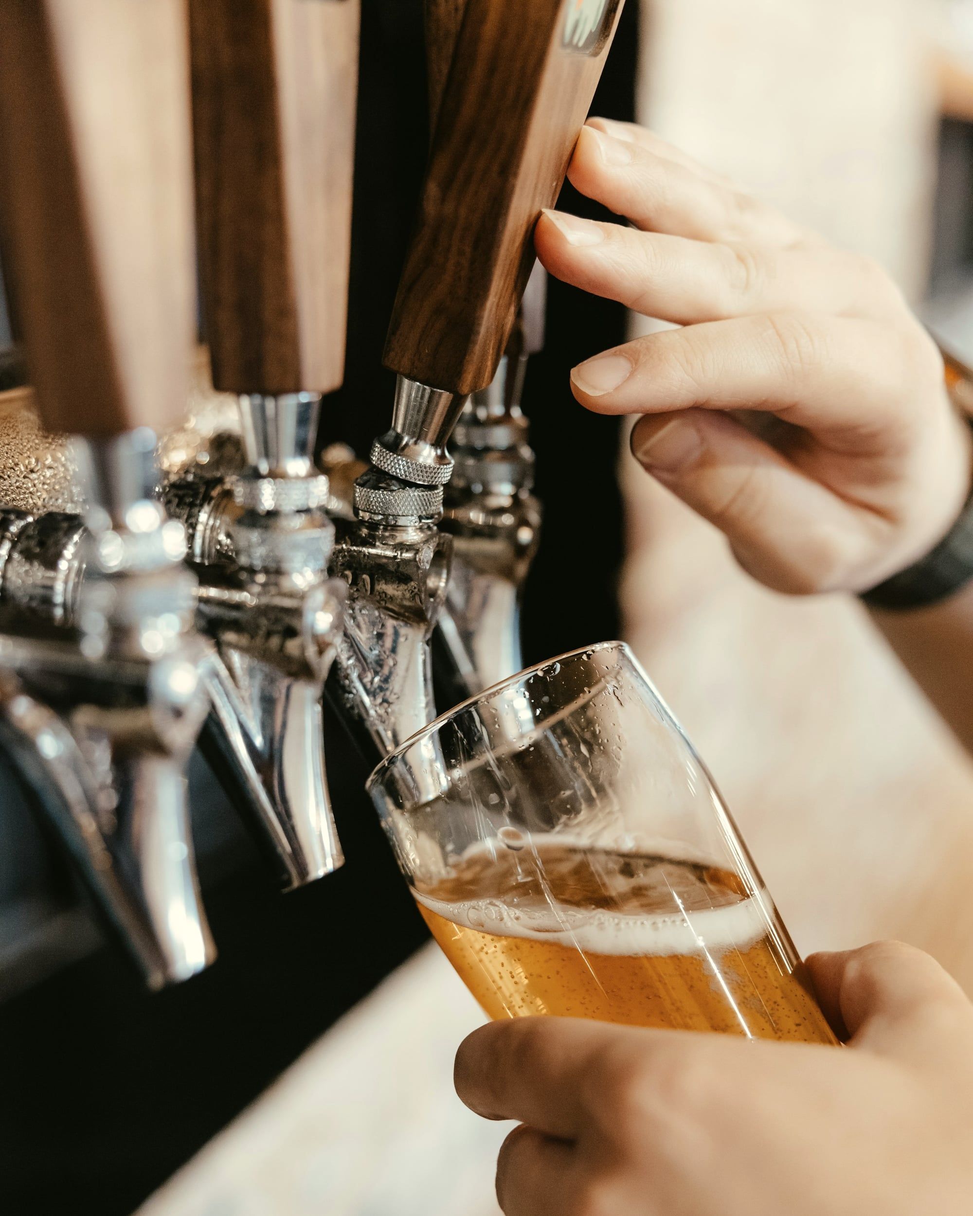 Eine Hand zapft Bier an einem Zapfhahn mit Holzgriffen